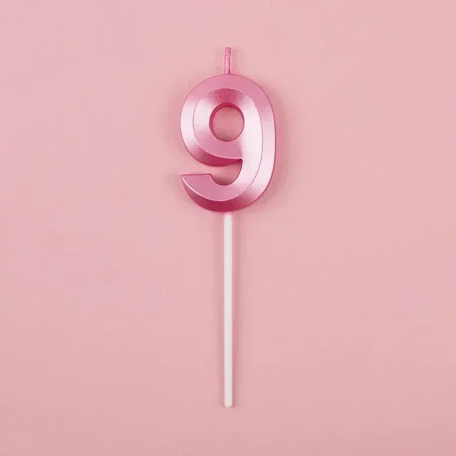 A pink number nine candle on a white stick against a light pink background.