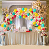 A floral and balloon arch decoration featuring pink, yellow, and blue balloons and flowers on a draped table.