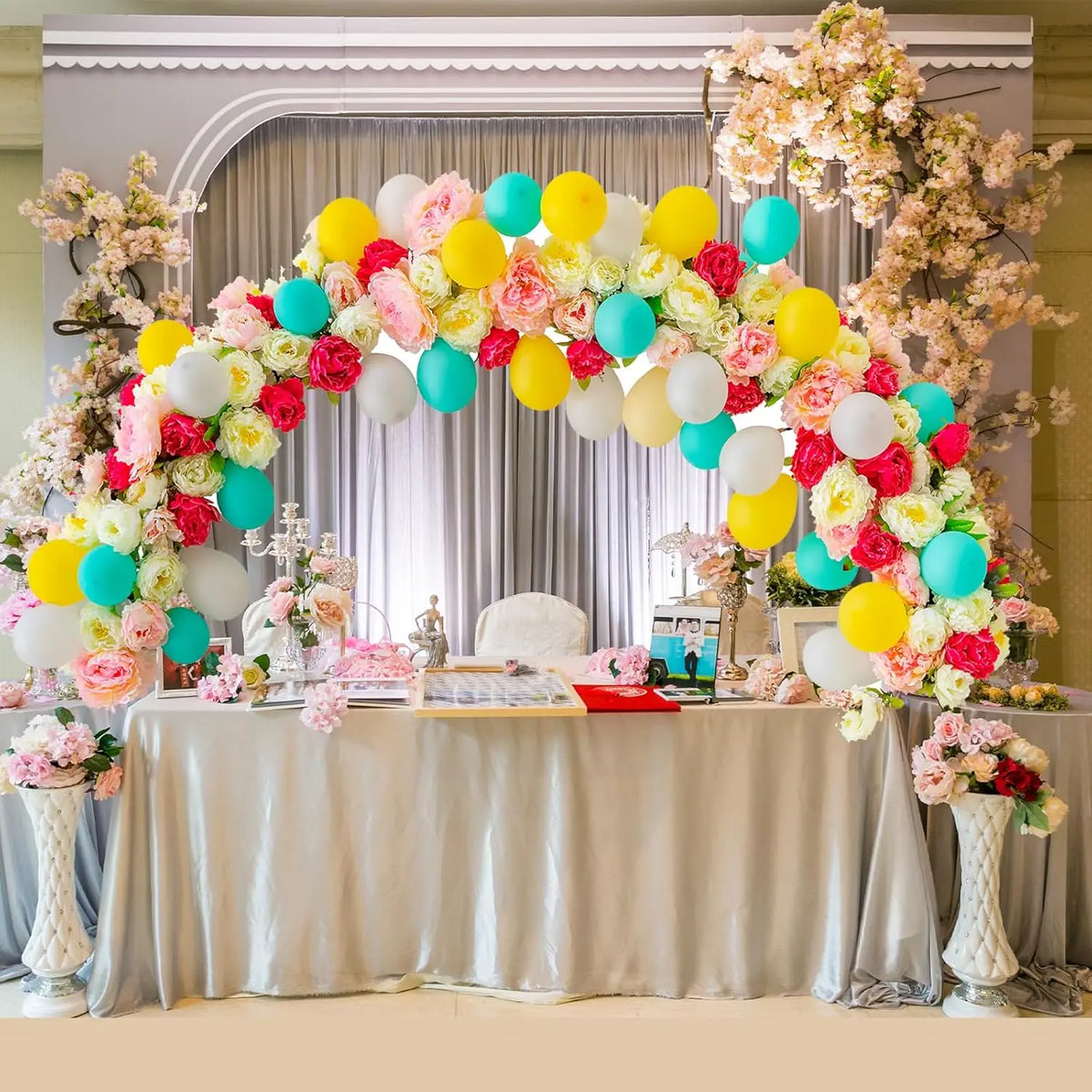 A floral and balloon arch decoration featuring pink, yellow, and blue balloons and flowers on a draped table.