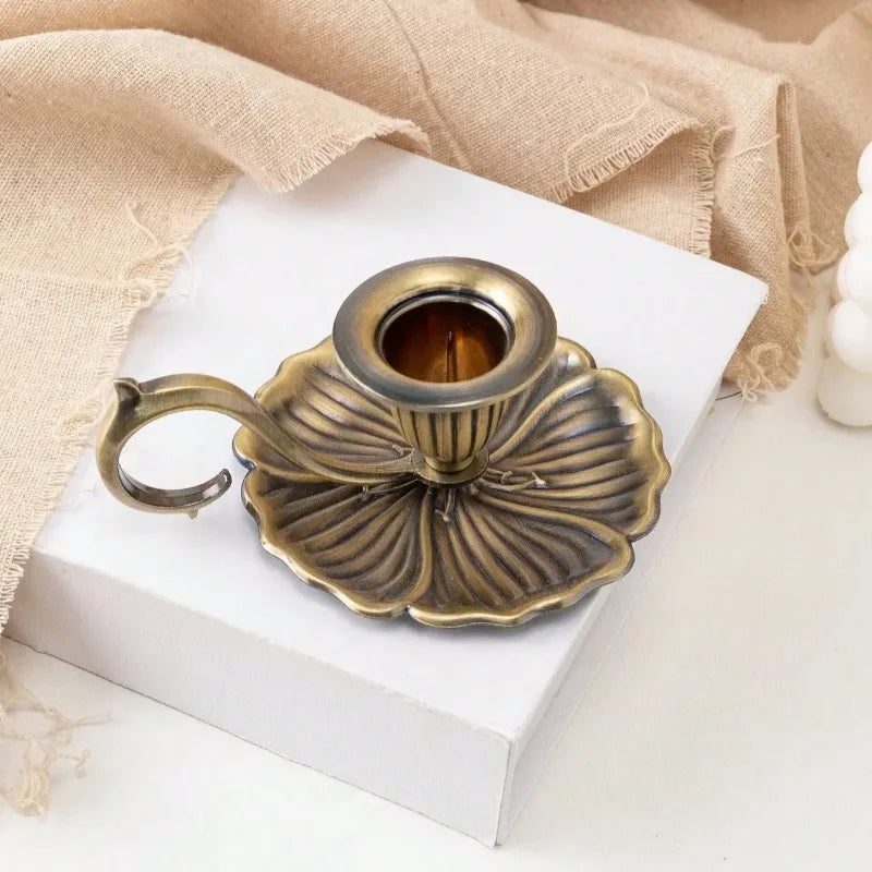 Un photophore en fer forgé vintage, en forme de lotus, sur une boîte blanche à côté d'un tissu en lin beige.