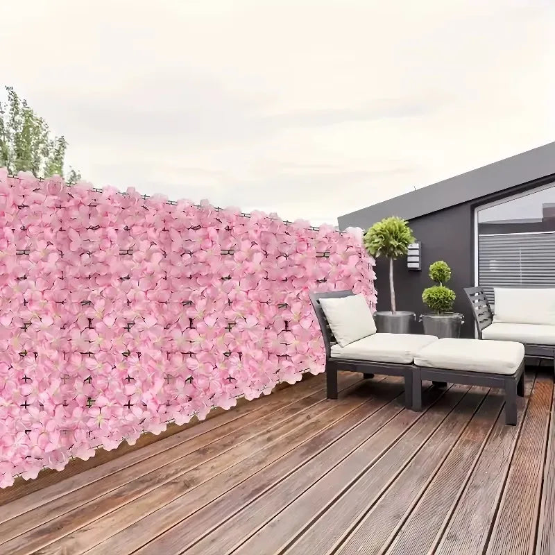 A pink artificial cherry blossom privacy fence screen next to a modern house with outdoor seating on a wooden deck.
