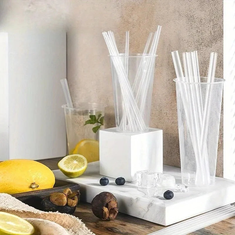 A clear glass container filled with transparent plastic drinking straws rests on a white marble surface.