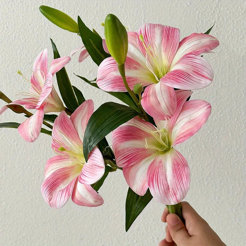Pink and white artificial lilies with green buds displayed in a hand
