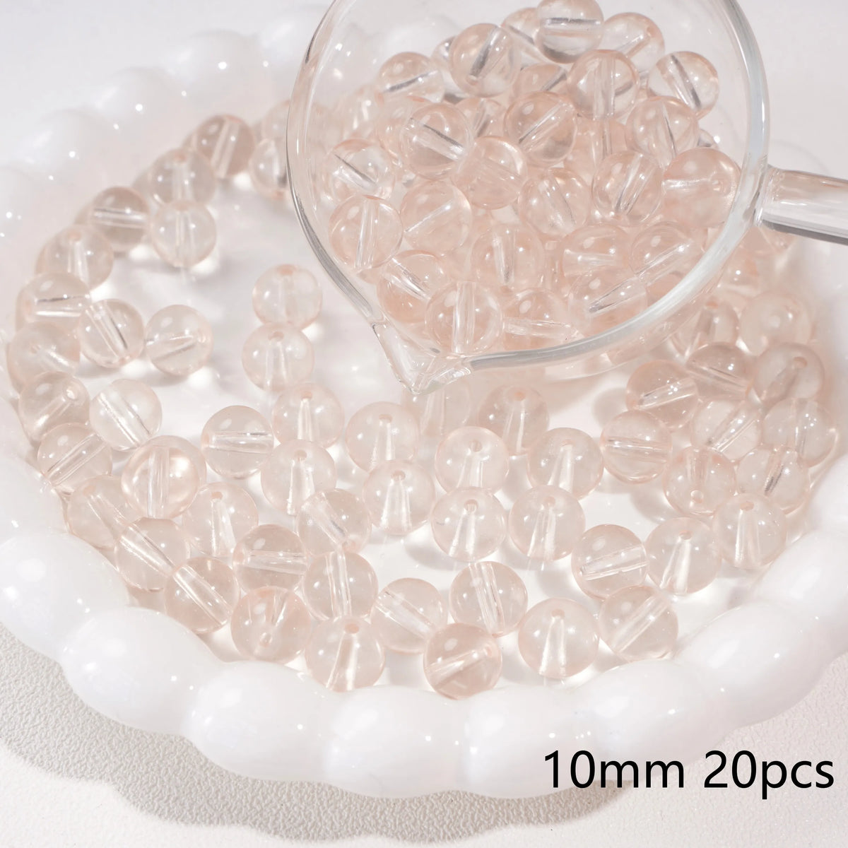 A small glass measuring cup filled with round, translucent pink spacer beads on a white dish.