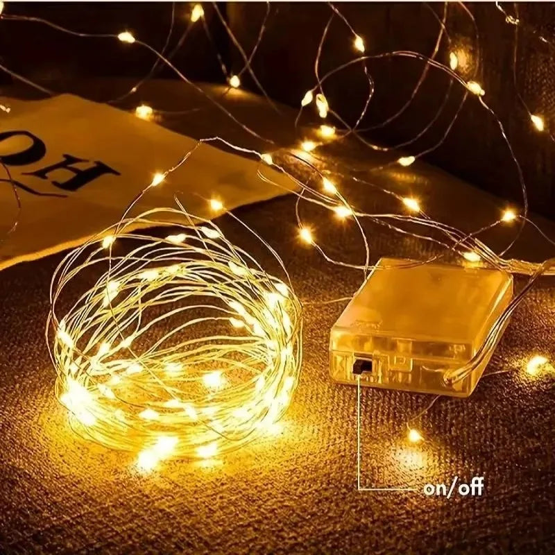 A bundle of warm yellow fairy string lights is displayed next to a battery pack on a dark surface.