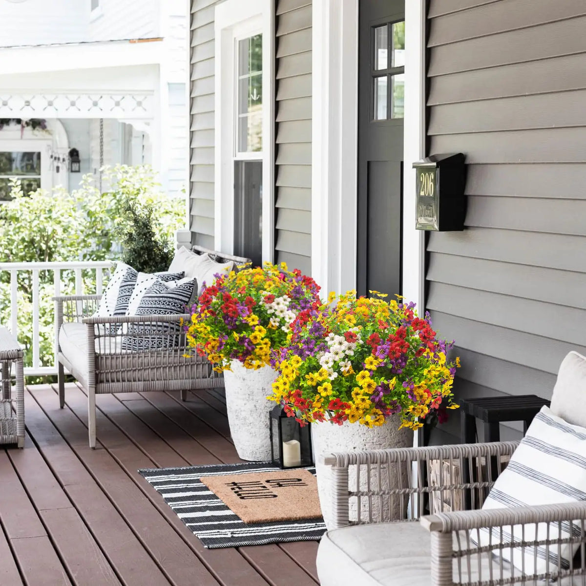 Topf mit künstlichen Frühlings-Nelkenblüten in Gelb, Lila und Rot auf einer Holzterrasse.