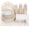 A set of gold polka dot disposable party tableware including plates and cups stacked on a white surface.