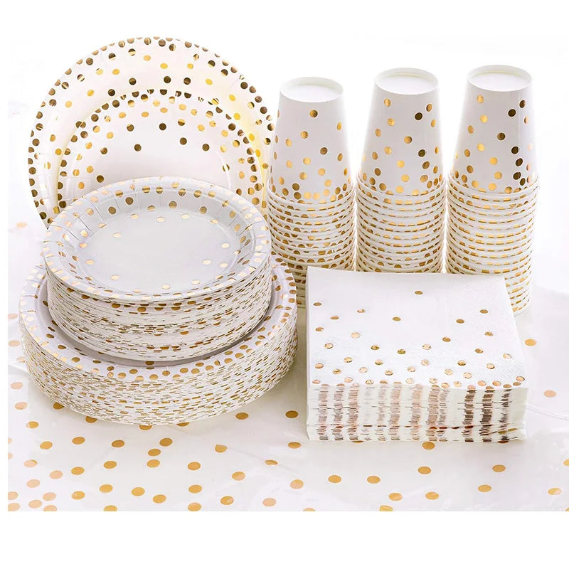 A set of gold polka dot disposable party tableware including plates and cups stacked on a white surface.