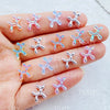 A hand displays various clear and iridescent balloon puppy nail art charms on the fingernails.