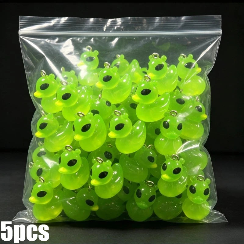 A clear plastic bag filled with numerous bright lime green glow-in-the-dark resin charms shaped like aliens and ducks.