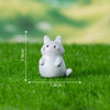 A small white cat figurine sitting on green grass with dimension markings.