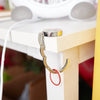 A silver foldable handbag hook is attached to a white wooden table leg.