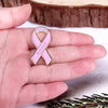 Un pin de esmalte rosa de concienciación sobre el cáncer de mama sostenido en la mano de una persona contra una superficie de