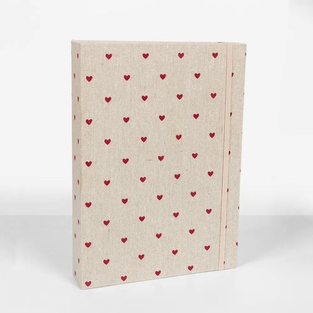 Álbum de scrapbooking de tela beige con un patrón de corazón rojo en la cubierta.