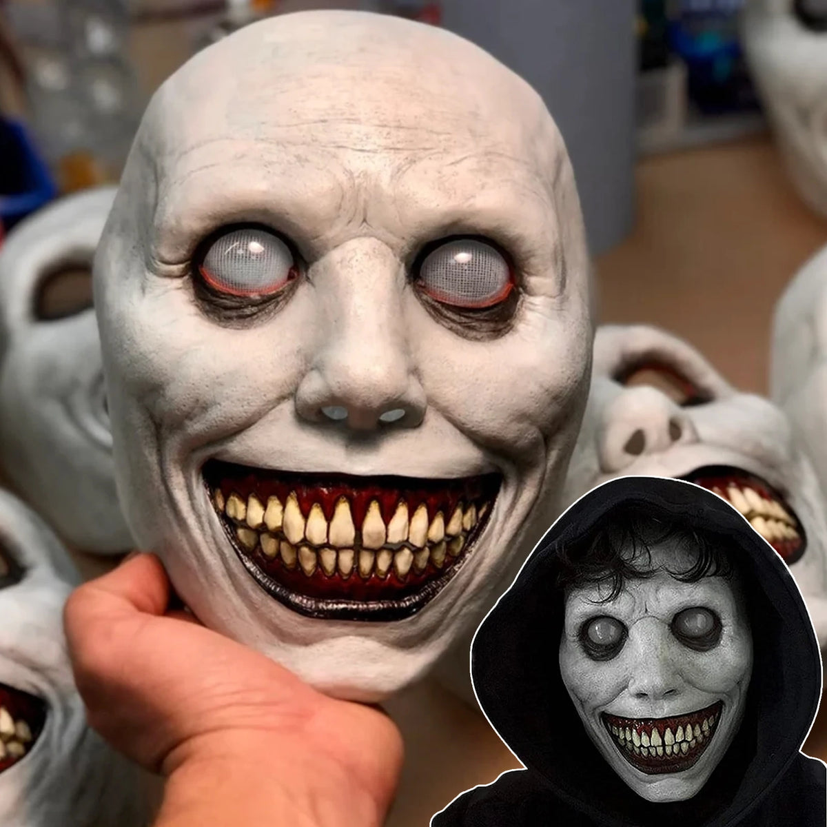 A close-up of a white demon mask with glowing red eyes and a wide, menacing smile being held by a hand.
