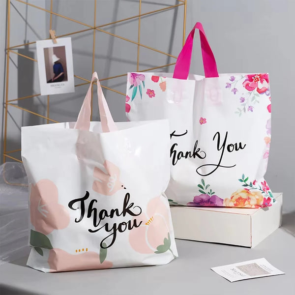 White floral thank you gift bags with pink handles displayed on a light gray surface.