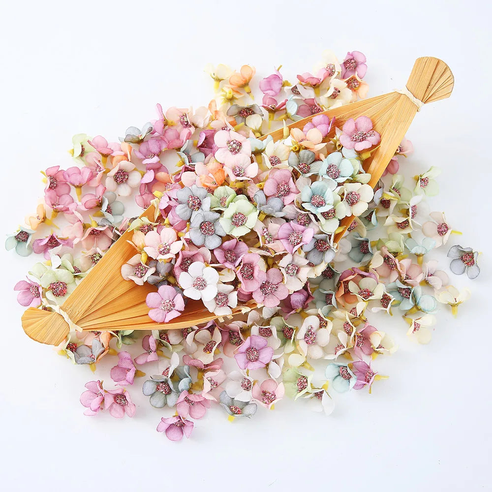 A collection of silk artificial flower heads in shades of pink, blue, and cream are displayed on a wooden paddle.