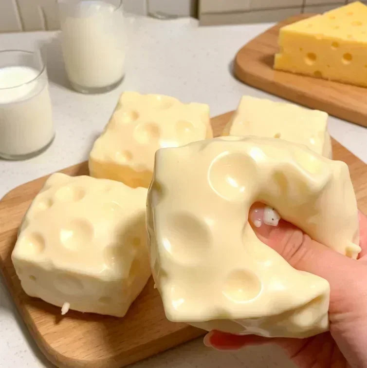 A hand holds a white, squishy cat paw shaped mochi toy on a wooden board with milk and cheese visible in the background.