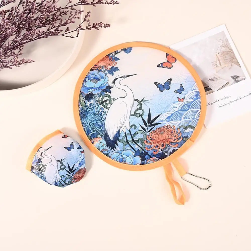 A circular fabric fan with a white bird design and butterfly accents is shown next to its folded form.