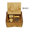 A wooden box containing a brass music box with a decorative lid featuring anime characters.
