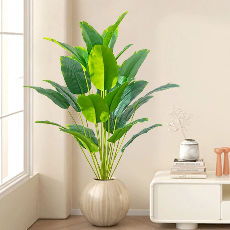 Artificial tropical palm tree with large green monstera leaves in a light colored vase