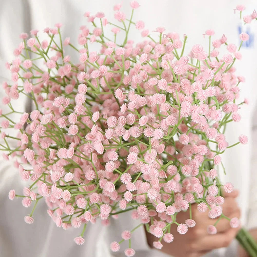 A bouquet of pink artificial gypsophila flowers with delicate green stems being held by a person.
