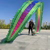 Una mujer realizando una danza de dragón con un gran accesorio de tela verde y morada colorido al aire libre.