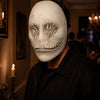 A person wearing a sculpted white ghost face mask in an indoor setting.