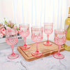 A set of elegant pink plastic wine glasses displayed on a wooden tray near a window.