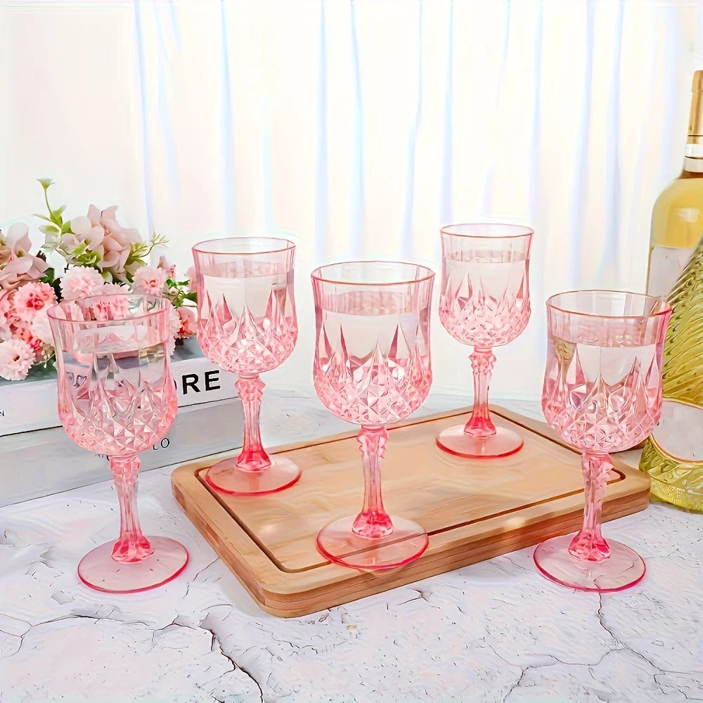 A set of elegant pink plastic wine glasses displayed on a wooden tray near a window.