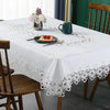 White embroidered lace tablecloth set for a dining table with floral accents and wooden chairs.