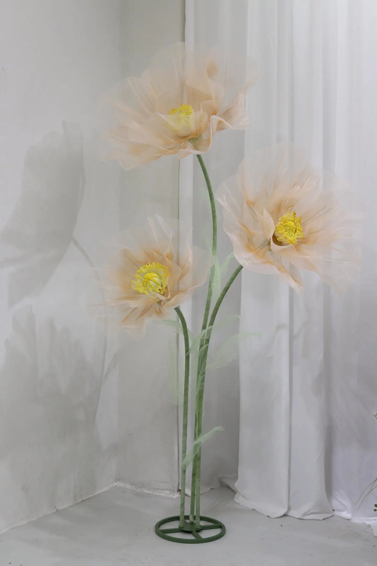A large artificial silk poppy flower with pale peach petals is displayed on a green stand against a white background.
