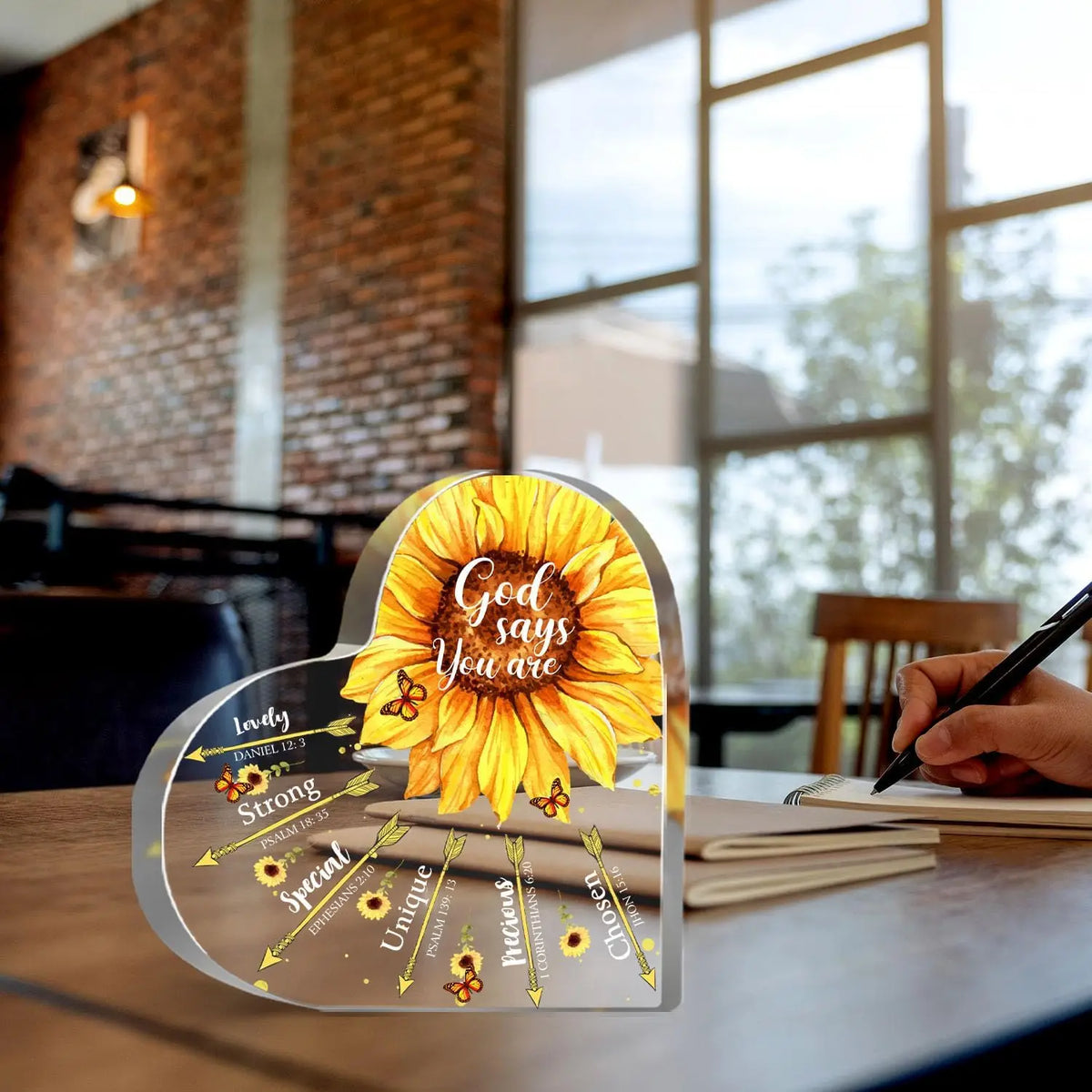 A heart-shaped sunflower plaque with Bible verses engraved on it rests on a wooden table.