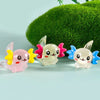 A set of colorful mini resin axolotl figurines in pink, white, and blue are displayed against a green moss background.