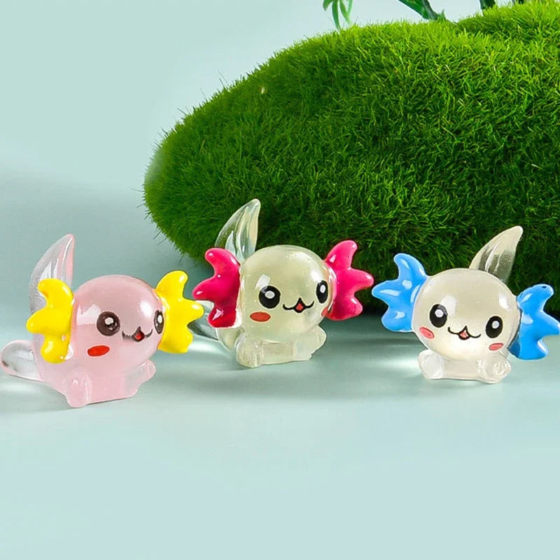A set of colorful mini resin axolotl figurines in pink, white, and blue are displayed against a green moss background.