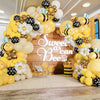 A yellow and black bee balloon garland decoration featuring honeycomb shapes and white flowers on a wooden background.