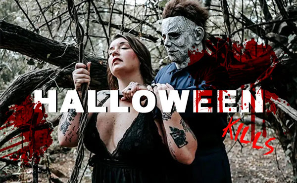 A woman holding a bloody horror mask resembling Michael Myers in a dark, wooded setting.