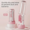 A clear plastic storage case holds a white electric baby bottle cleaning brush with multiple bristles.