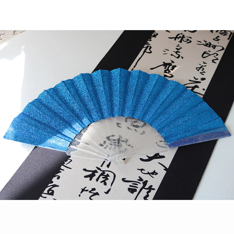 A blue glitter folding fan with transparent ribs displayed against a dark background.