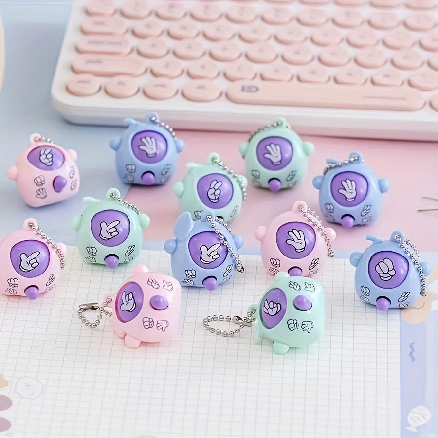 A collection of mini rock-paper-scissors themed keychains in purple, blue, and green are displayed on a white grid background