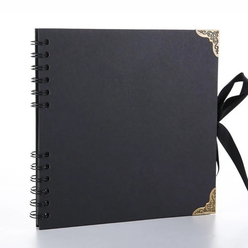 Bloc-notes d'album plat noir avec accents décoratifs dorés et un ruban noir attaché sur le côté.