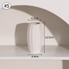 A white ceramic bud vase with vertical ribs is displayed on a shelf.