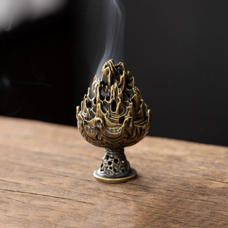 A vintage alloy incense burner holder with a textured, flame-like design emitting smoke on a wooden surface.
