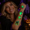 A smiling woman shows off glow-in-the-dark Halloween temporary tattoos on her arm in a dark, festive setting.