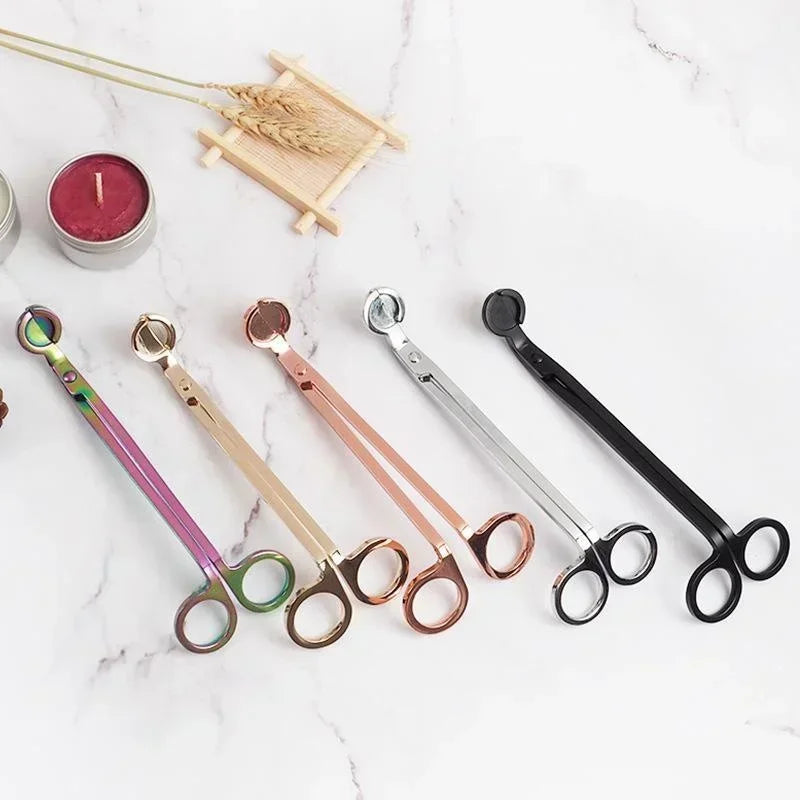 A collection of stainless steel candle wick trimmer scissors and a wooden tray on a white marble surface.