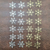 A collection of frosted snowflake confetti in silver and gold colors arranged in rows.