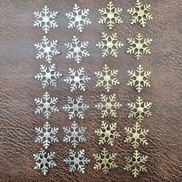 A collection of frosted snowflake confetti in silver and gold colors arranged in rows.