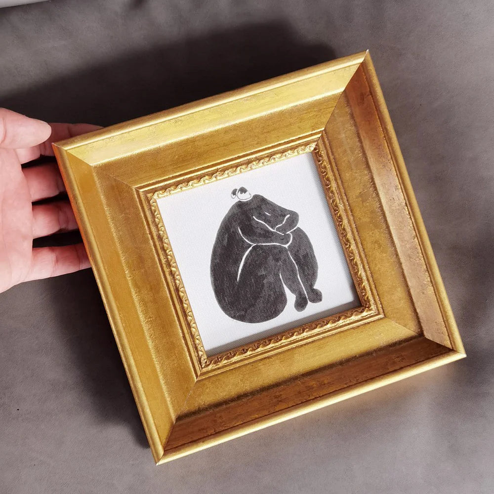 A hand holds an elegant gold photo frame with a black silhouette drawing inside.