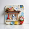 A white ceramic tray holds various kitchen items like a woven basket, wooden spoons, and colorful magnets.