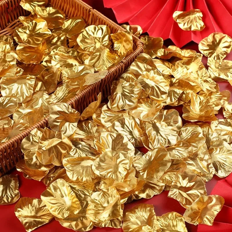 A pile of gold silk rose petals in a woven basket and scattered on red fabric.